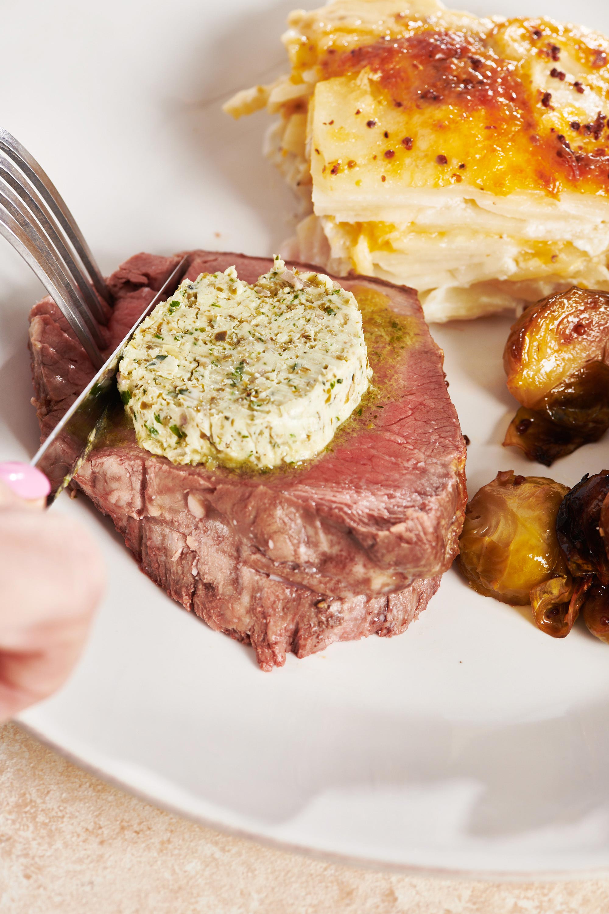 Cutting slice of Beef Tenderloin Roast with compound butter on plate.