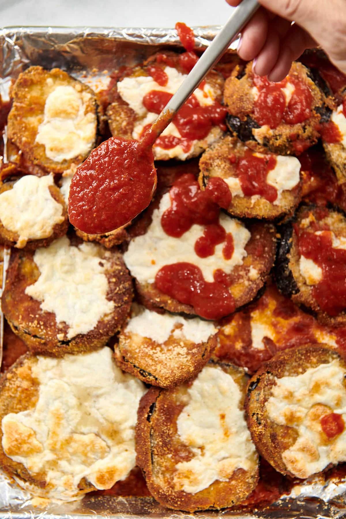 Spoon adding marinara sauce to Crispy Baked Eggplant Parmesan.
