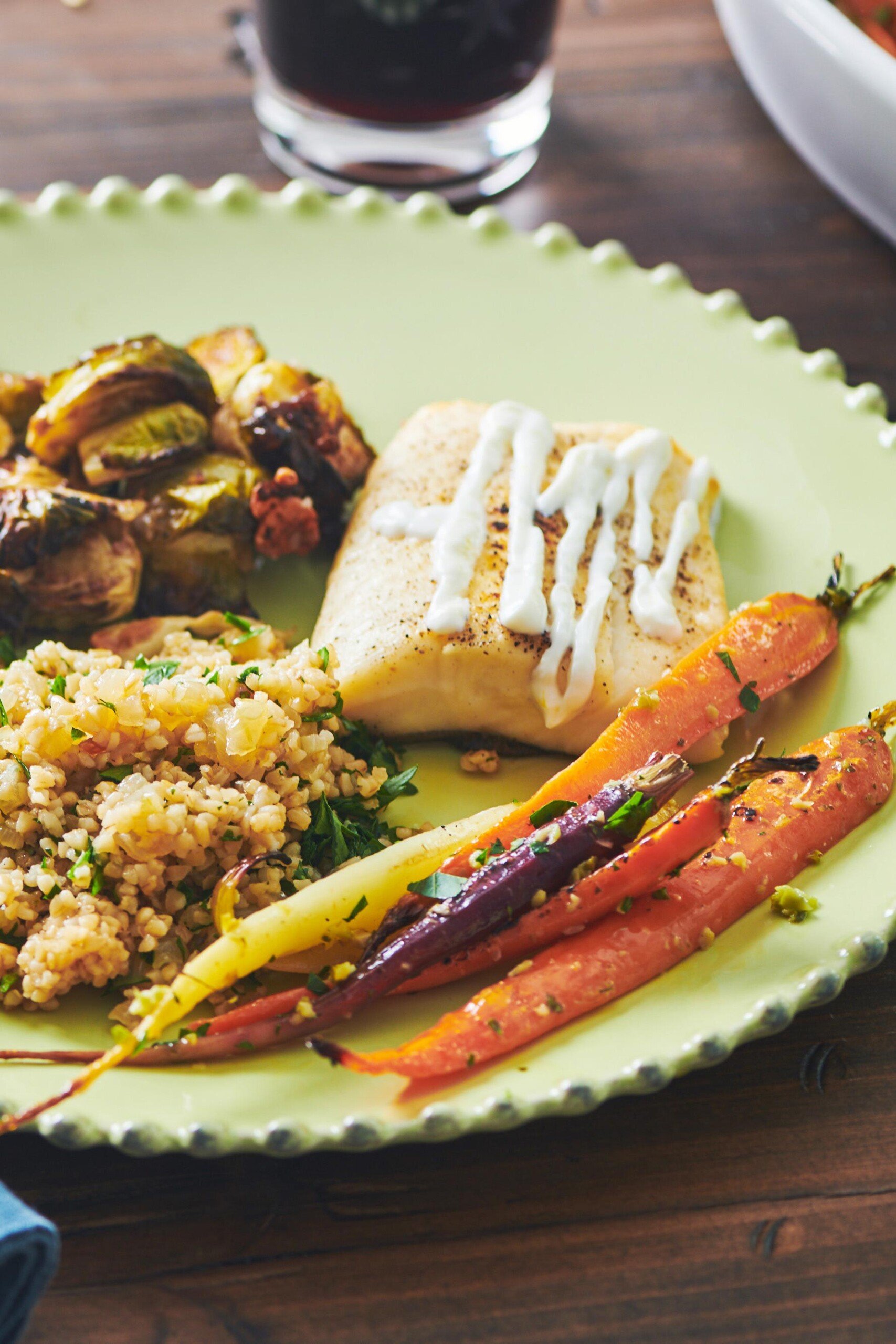 Roasted Cod with Lemon Yogurt Sauce on green plate with Brussels sprouts, carrots, and bulgur wheat salad.