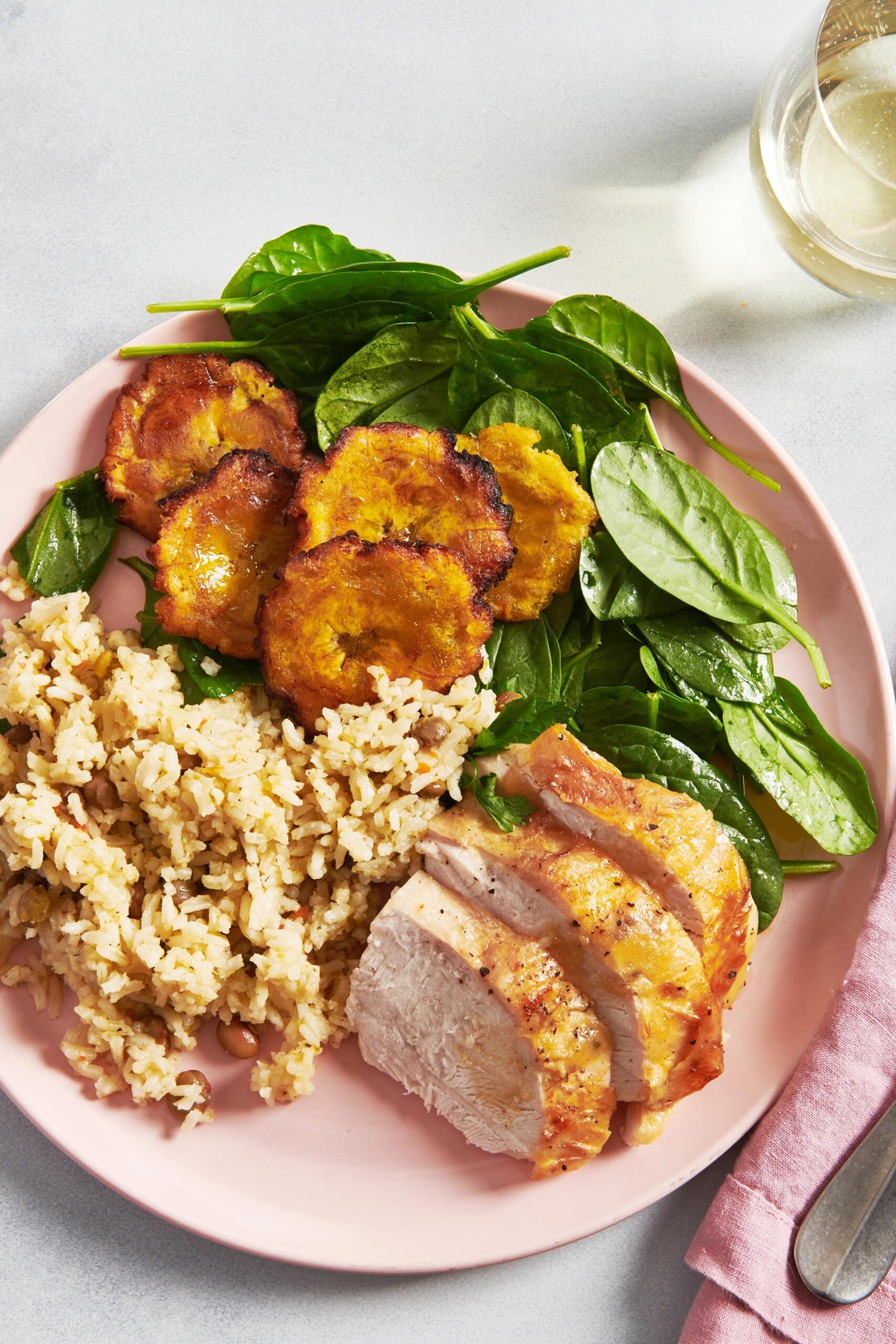 Tostones, spinach, rice, and meat on a pink plate.