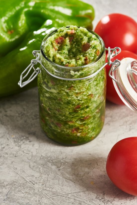 Glass jar of Sofrito on a counter with vegetables.