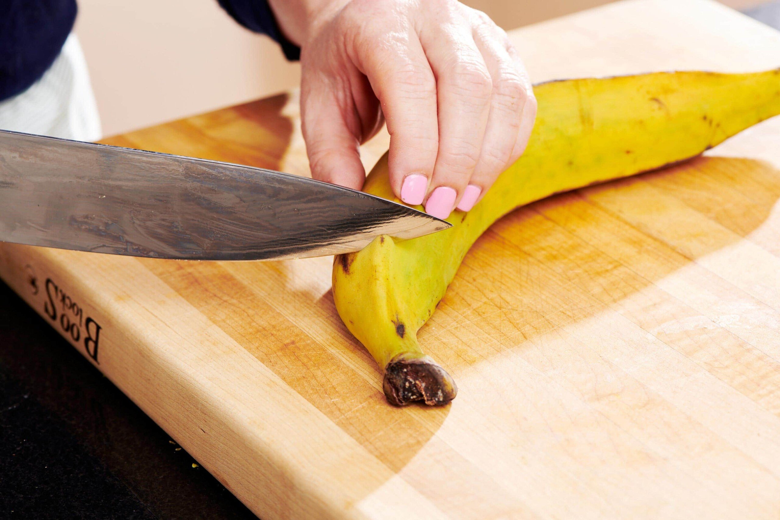 Woman slicing the end off of an unpeeled plantain.