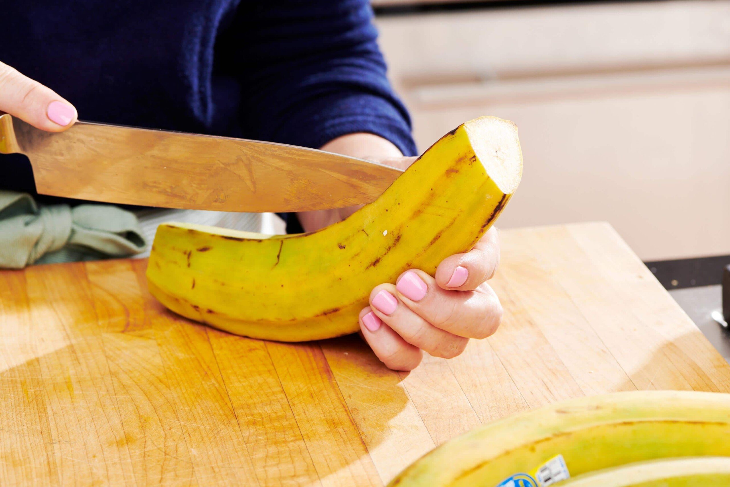 Woman using a knife to remove the peel from a plantain.