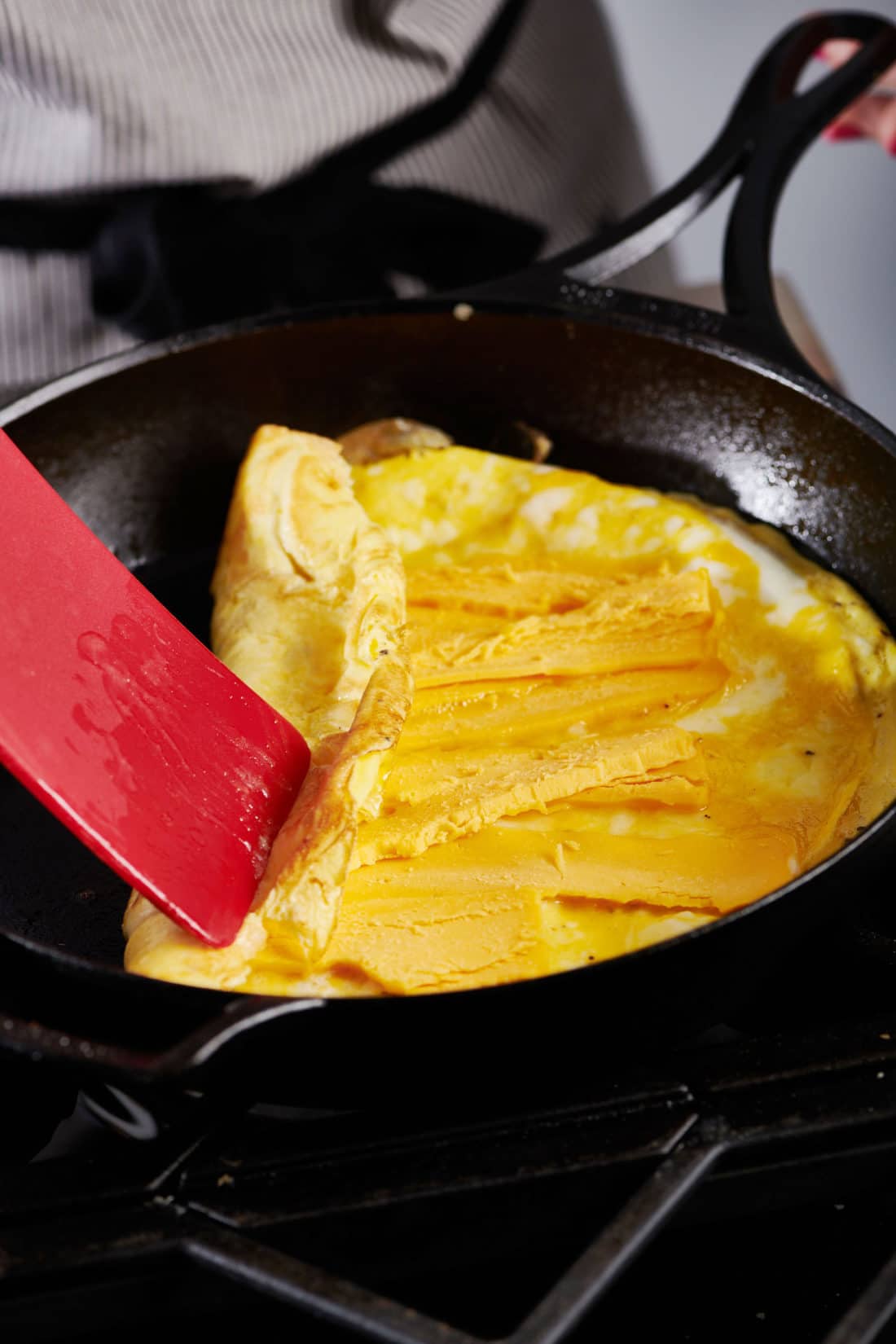 Red spatula folding cooked egg over cheese in a skillet.