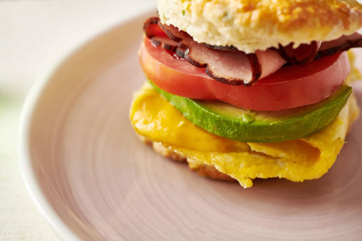 Breakfast sandwich with Cooper cheese, avocado, tomato, egg, and ham.