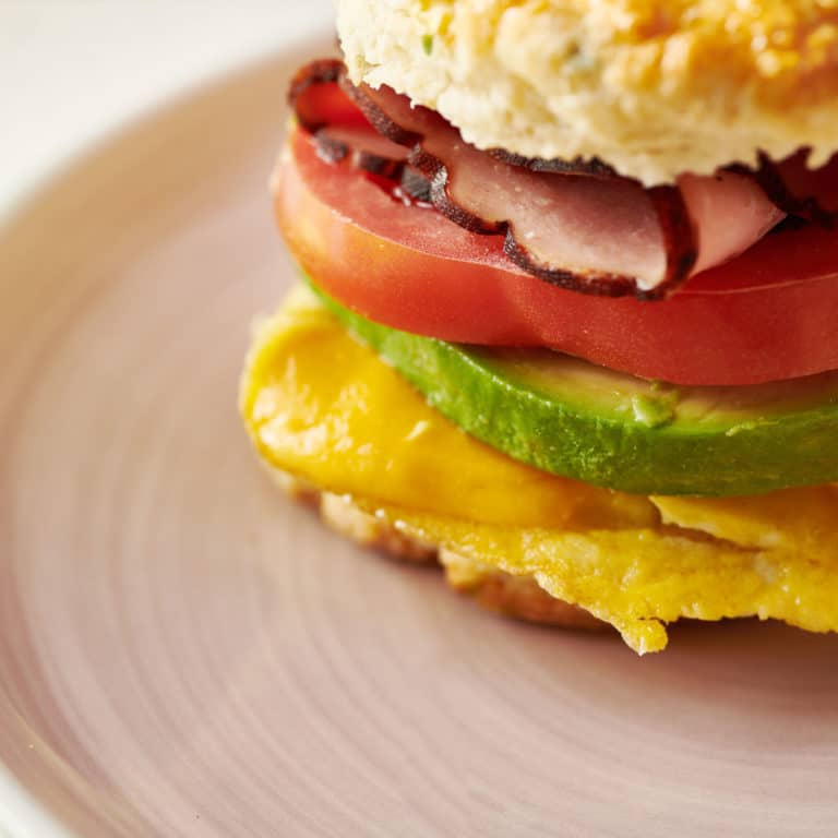 Breakfast sandwich with Cooper cheese, avocado, tomato, egg, and ham.