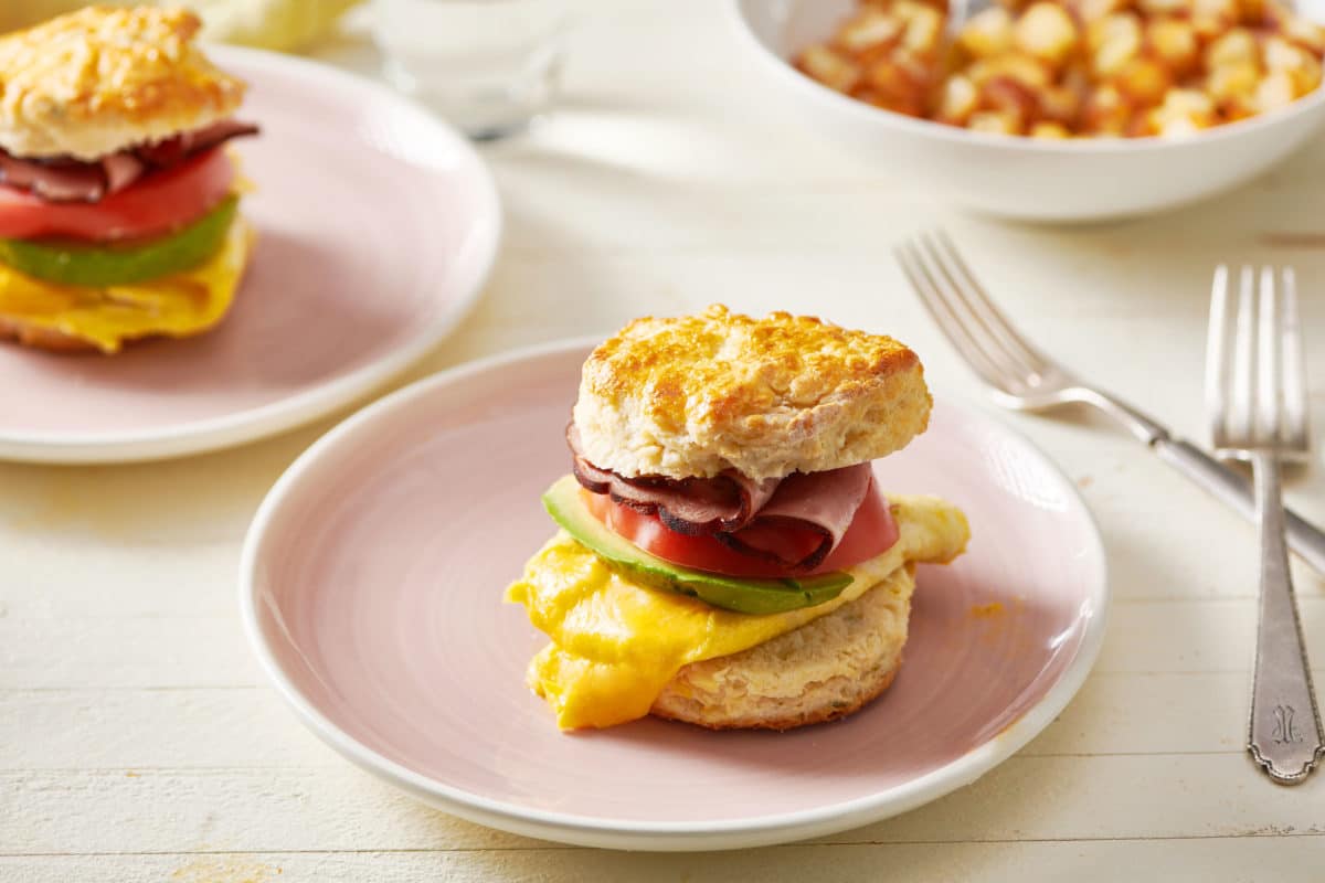 Biscuit Breakfast Sandwich with ham, tomato, avocado, Cooper cheese, and egg on a plate.