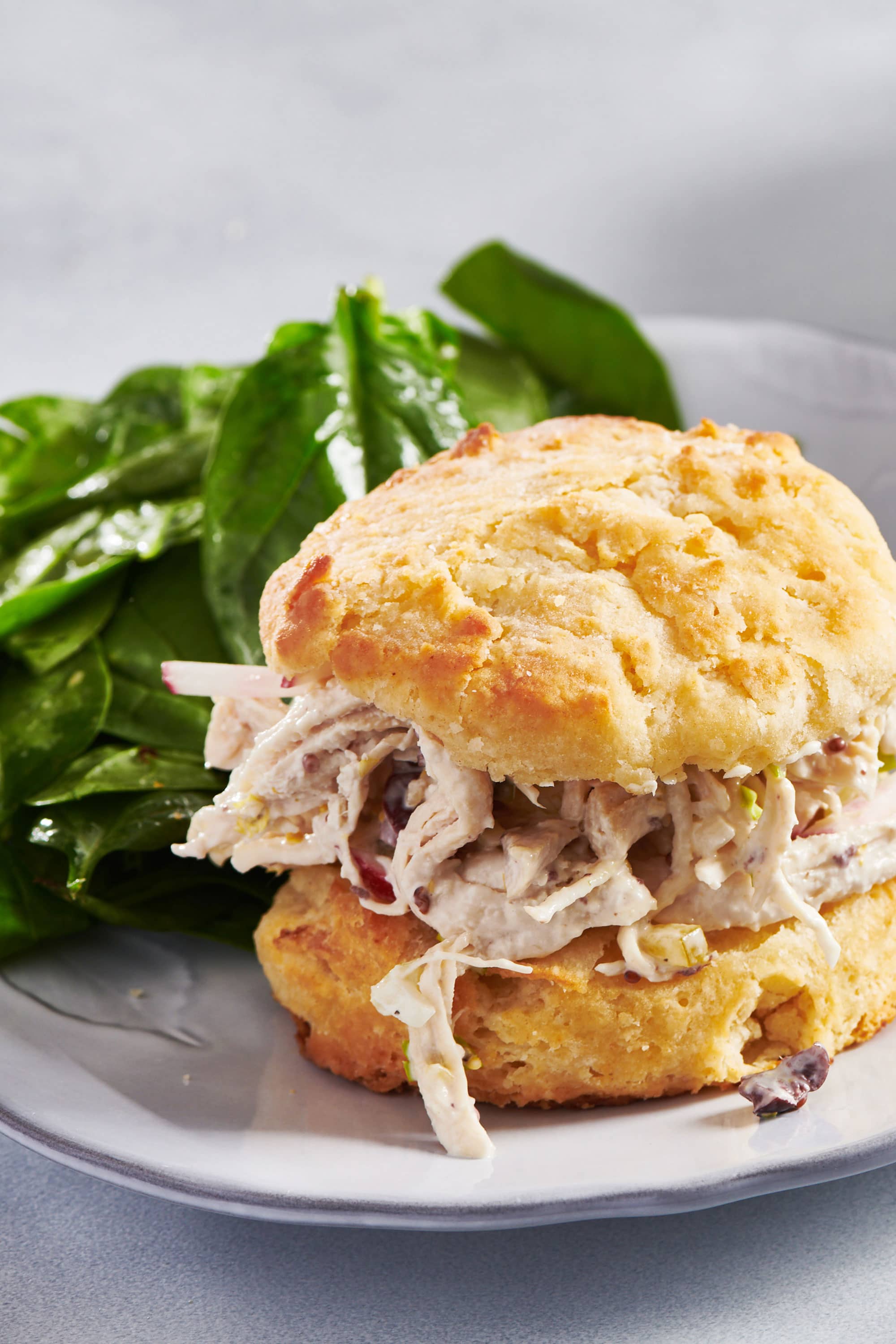 Best Chicken Salad in a biscuit sandwich on a plate with spinach salad.