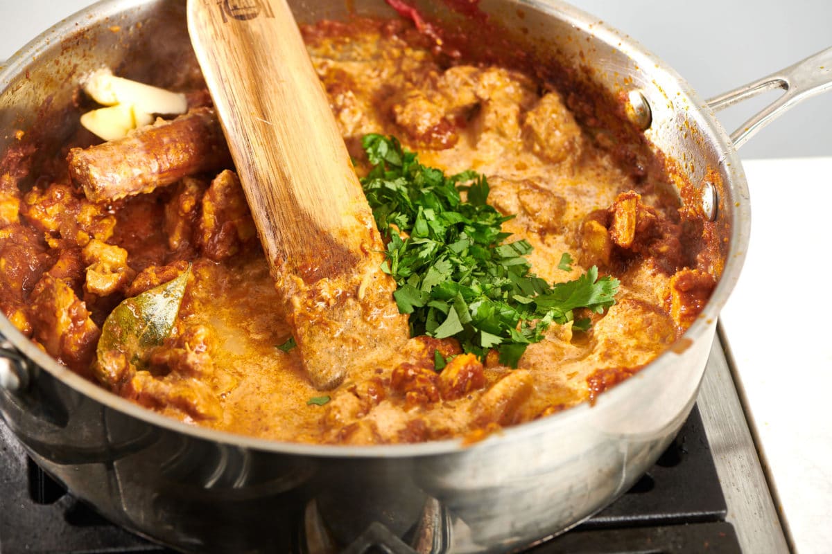 Wooden spatula stirring a skillet of Butter Chicken (Murgh Makhani).