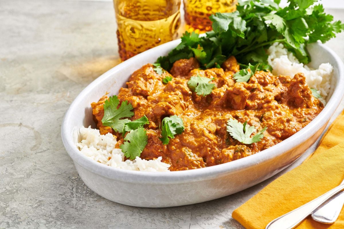 Baking dish of Butter Chicken (Murgh Makhani) and rice on a table.