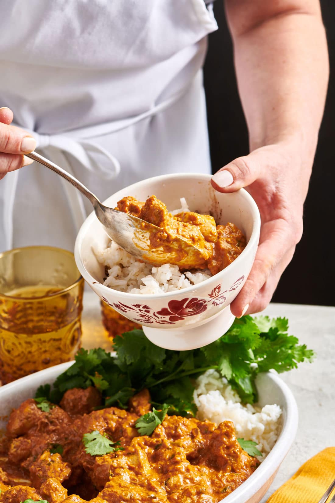 Woman scooping Butter Chicken (Murgh Makhani) into a bowl of rice.