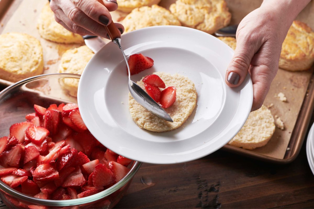Woman scooping strawberries onto a shortcake biscuit.