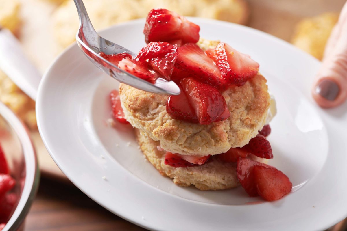 Spoon putting strawberries onto biscuits with whipped cream and strawberries.