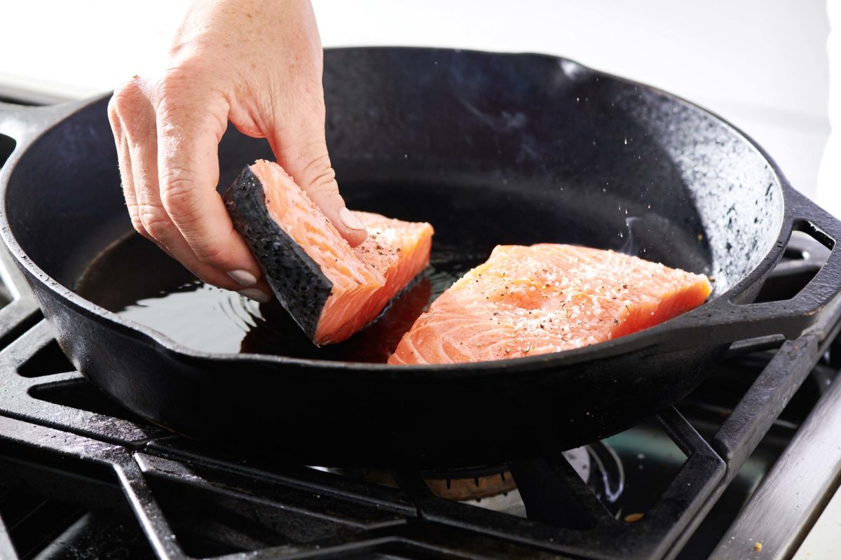 Woman placing salmon in a skillet.