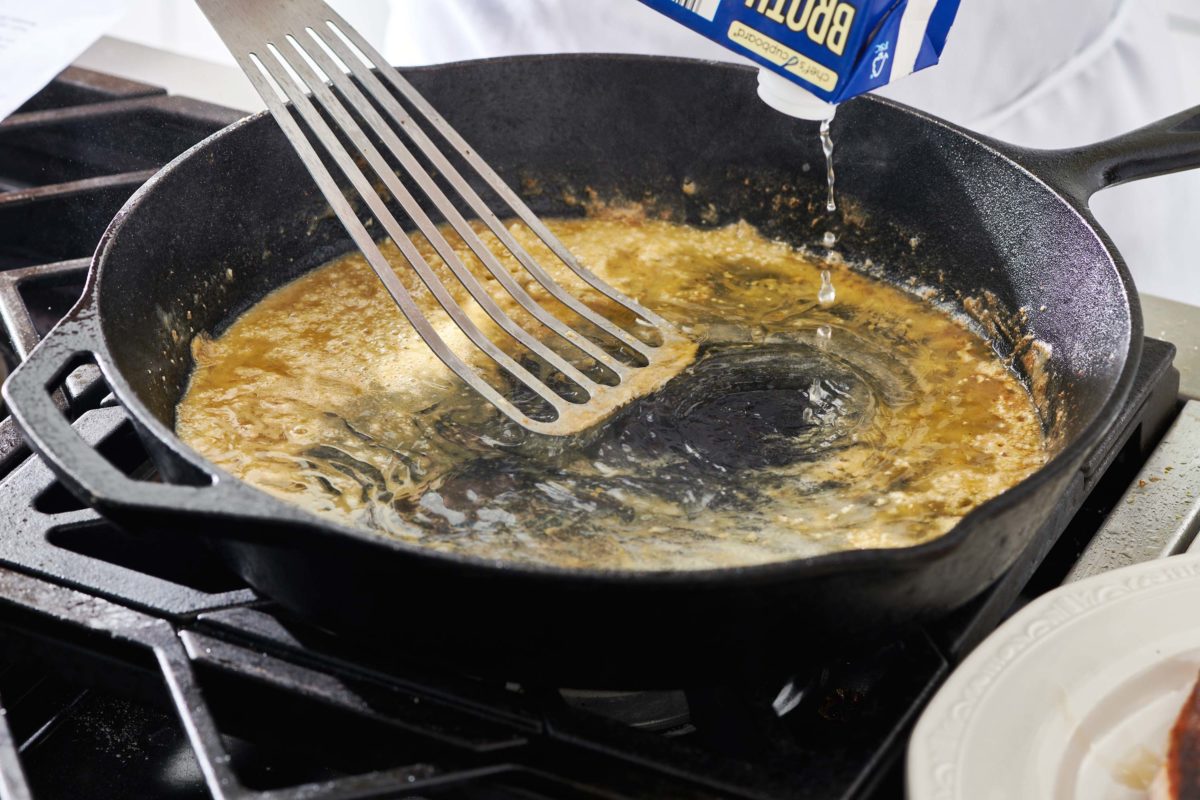 Broth pouring into a skillet with a metal spatula.