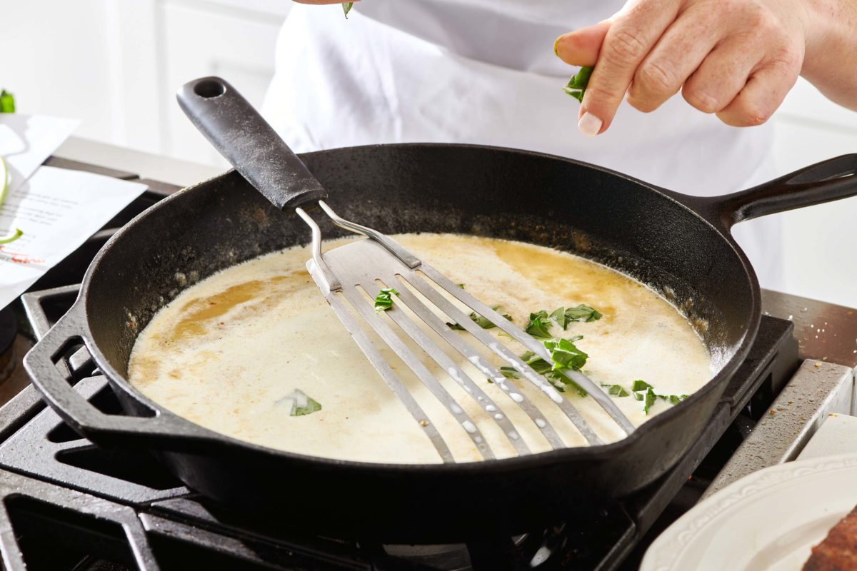 Woman adding herbs to a skillet.