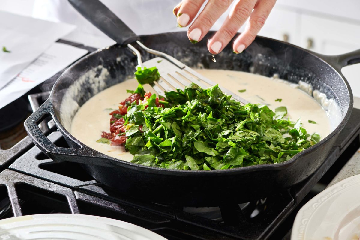Pile of spinach in a skillet with a creamy broth mixture.