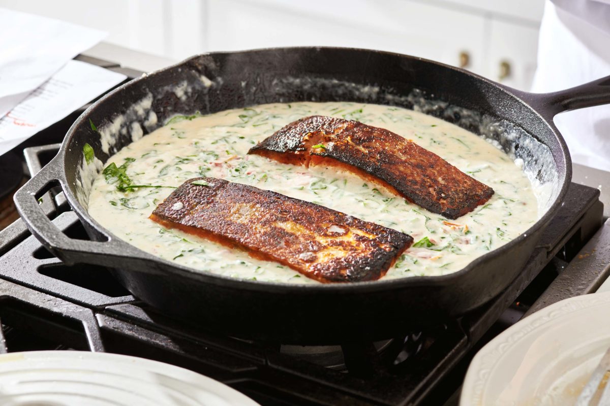 Salmon in a skillet of creamy broth mixture.