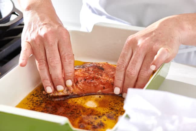 Woman coating salmon in a mixture of seasonings and olive oil.
