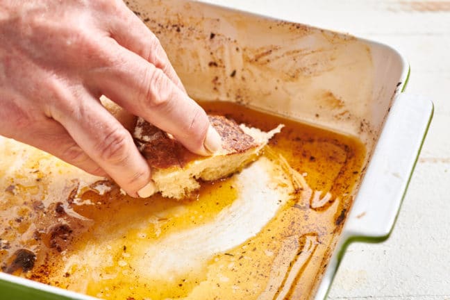 Woman dipping bread into pan juices.