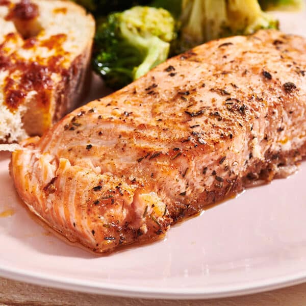 Herbed salmon filet on pink plate with side dishes.