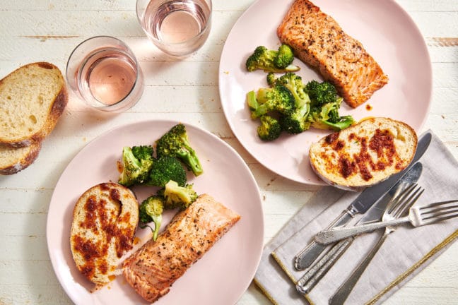 Two plates of Herbed Salmon, broccoli, and bread.