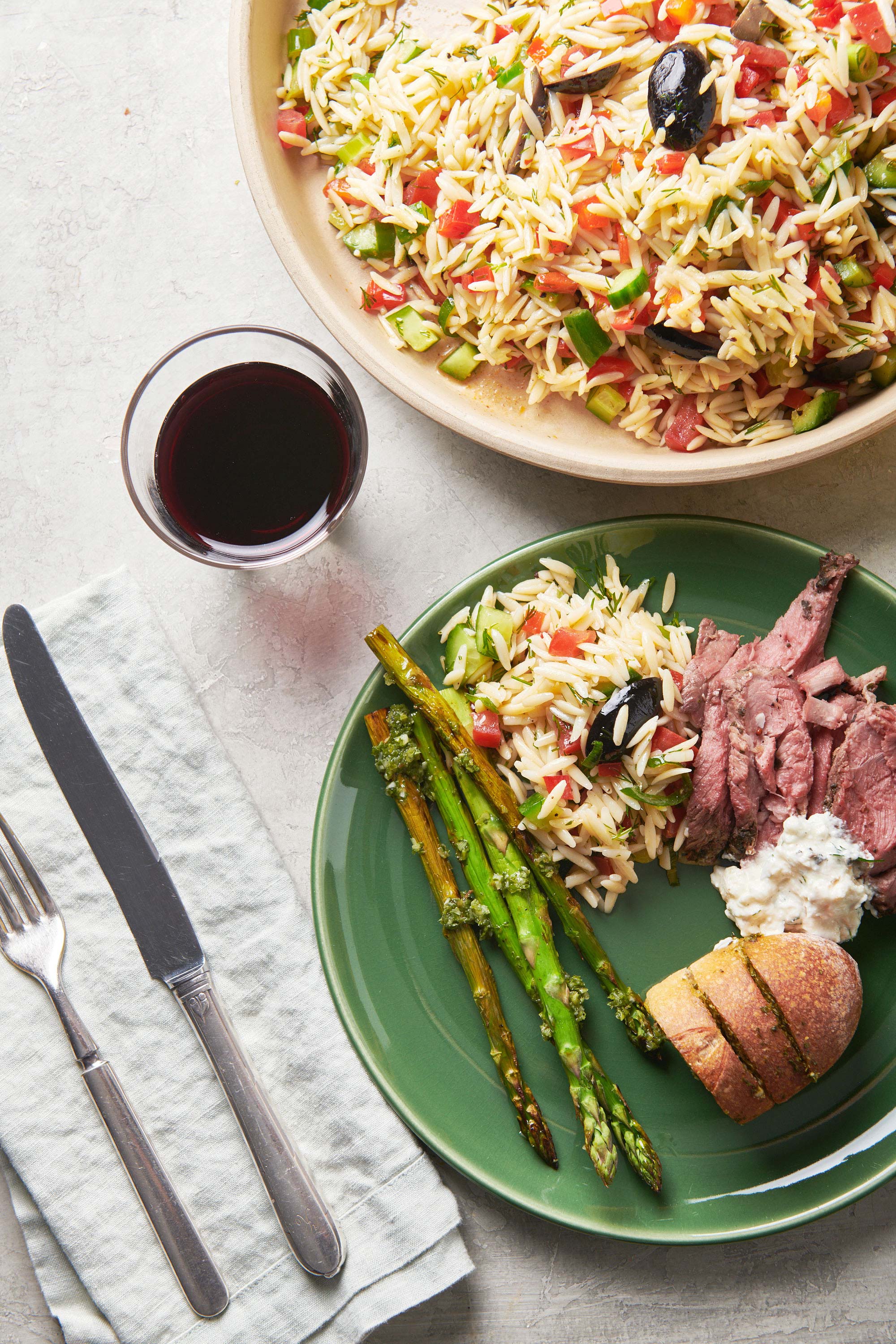 Greek Orzo Salad on a plate with asparagus, bread, and meat.