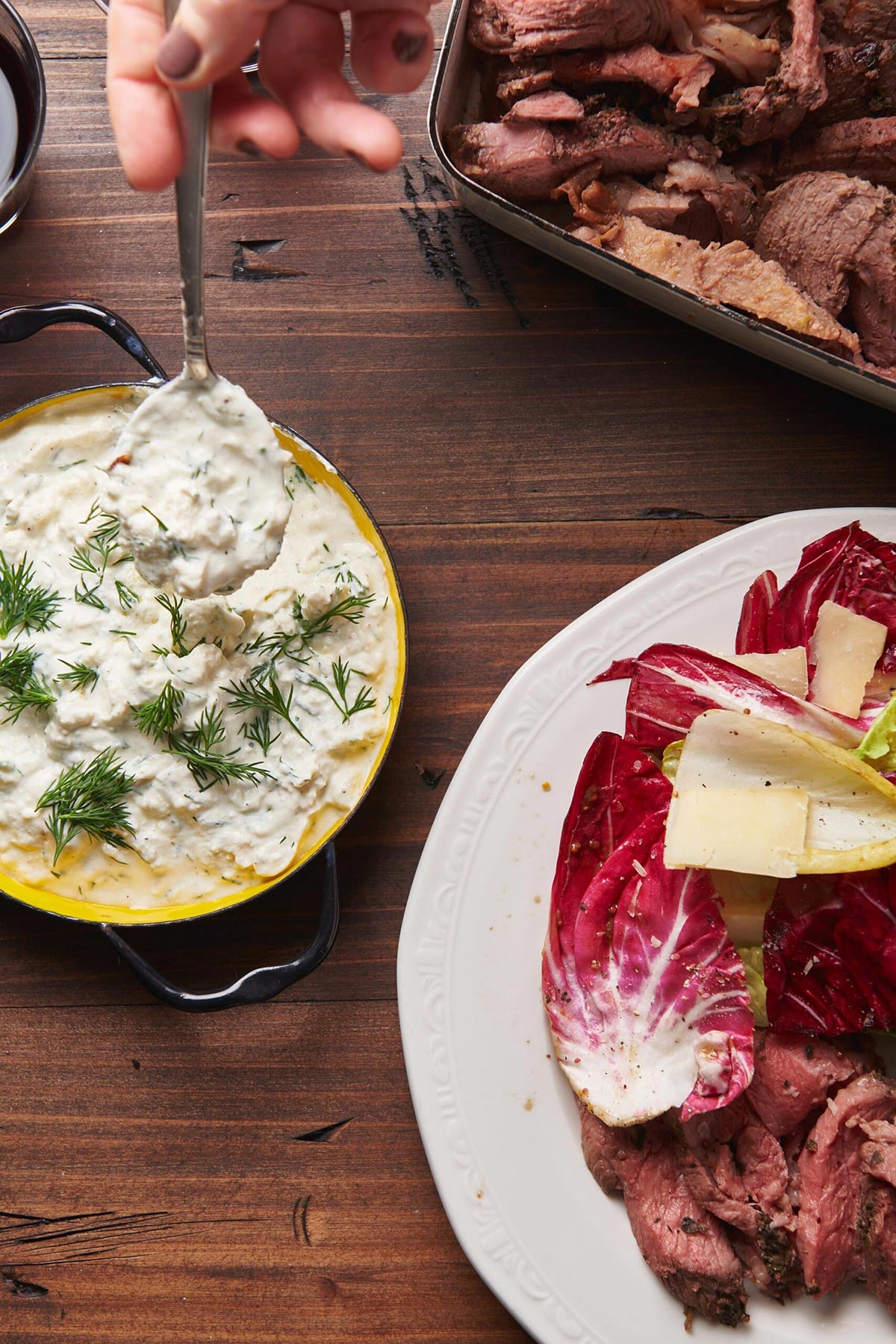 Serving Feta Sauce with spoon alongside lamb and cabbage.
