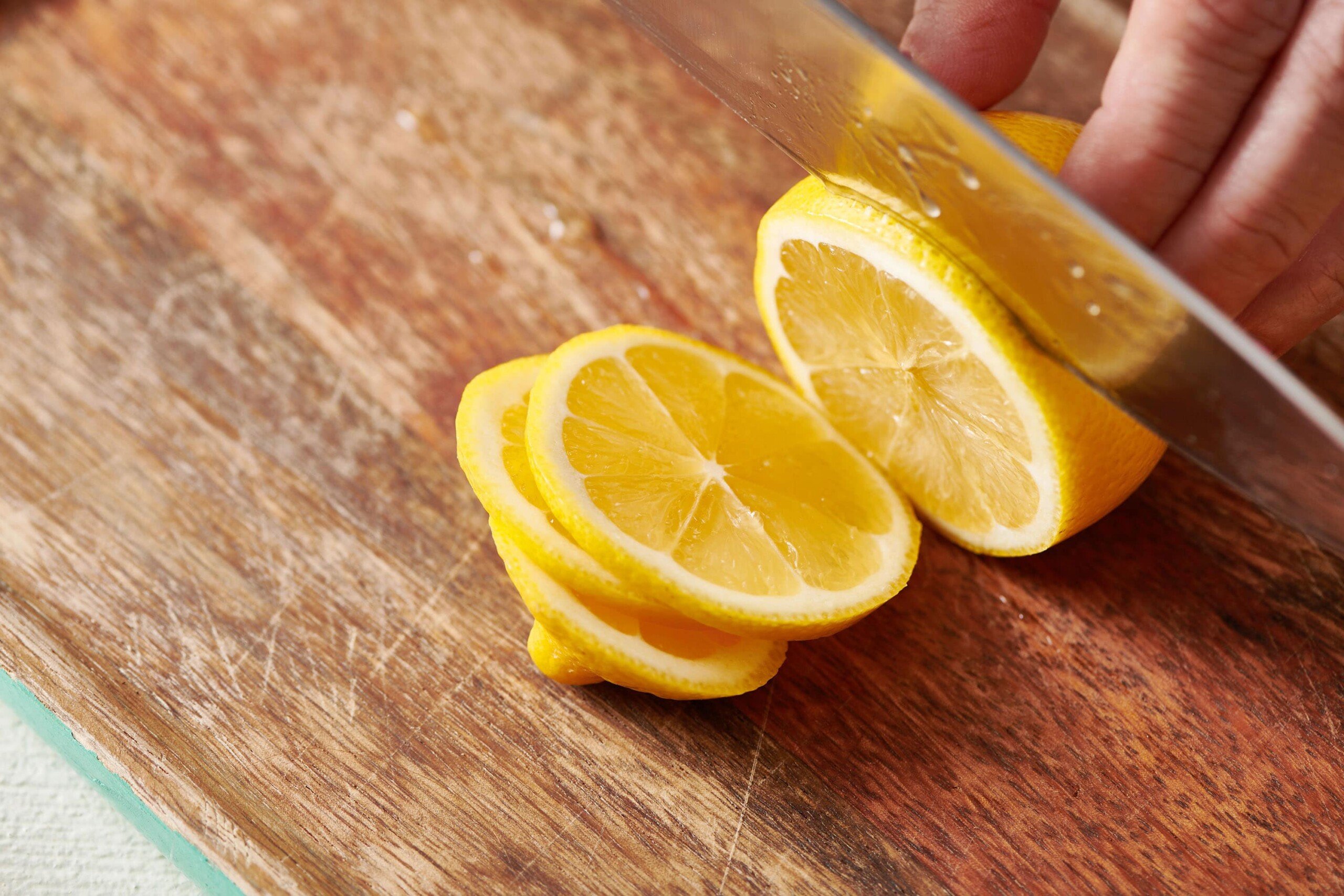 Partially sliced lemon on a wooden cutting board.