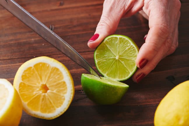 Woman halving a lime with a knife.