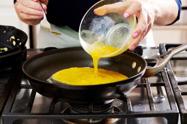 Woman pouring beaten eggs into a skillet.