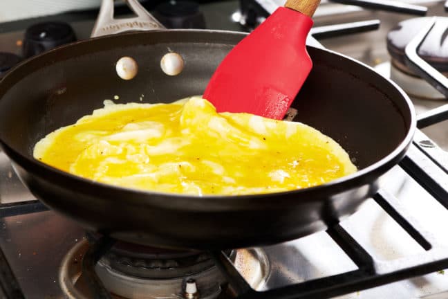 Red spatula lifting the edge of omelet from a skillet.