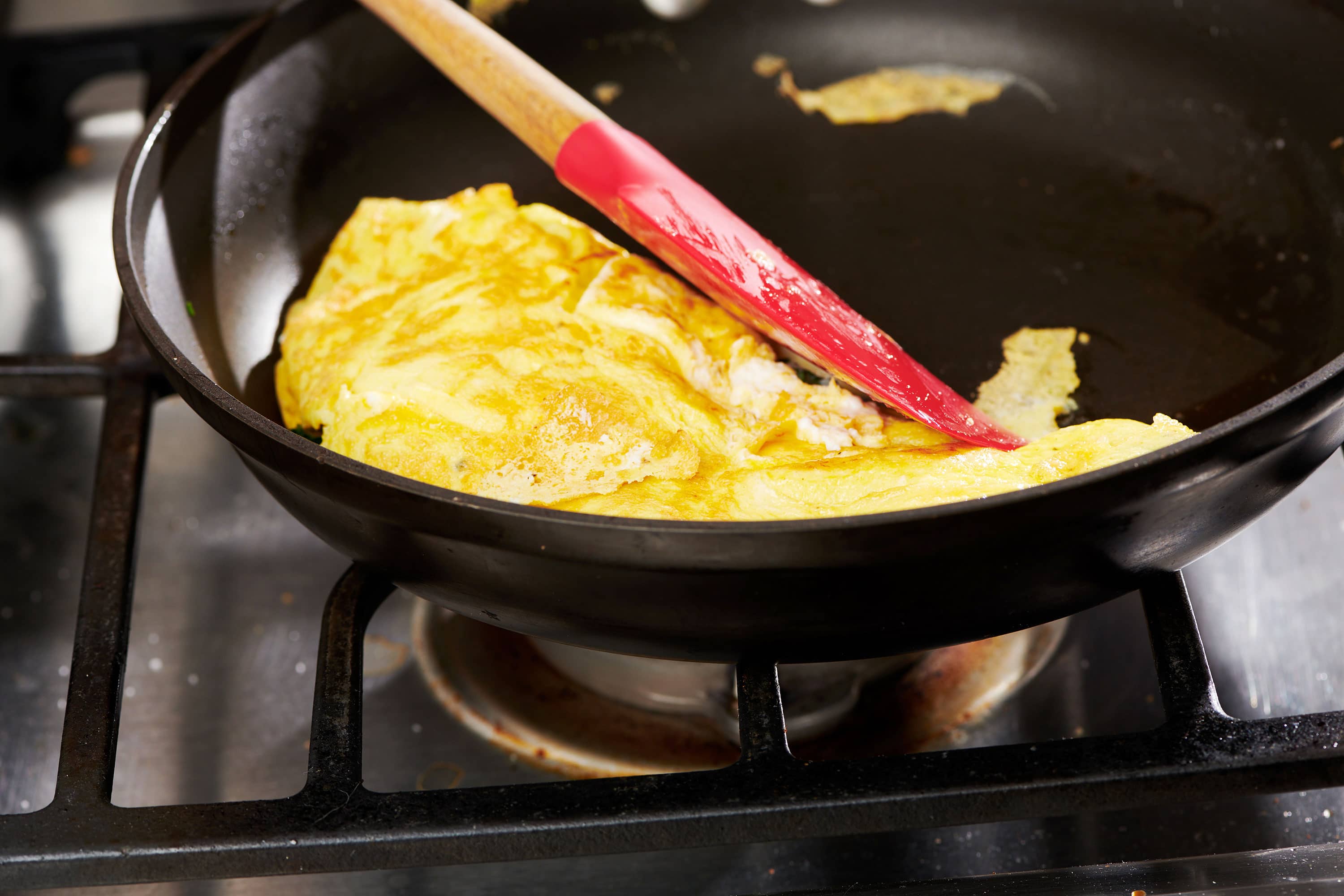 Folding omelet in pan with red spatula.