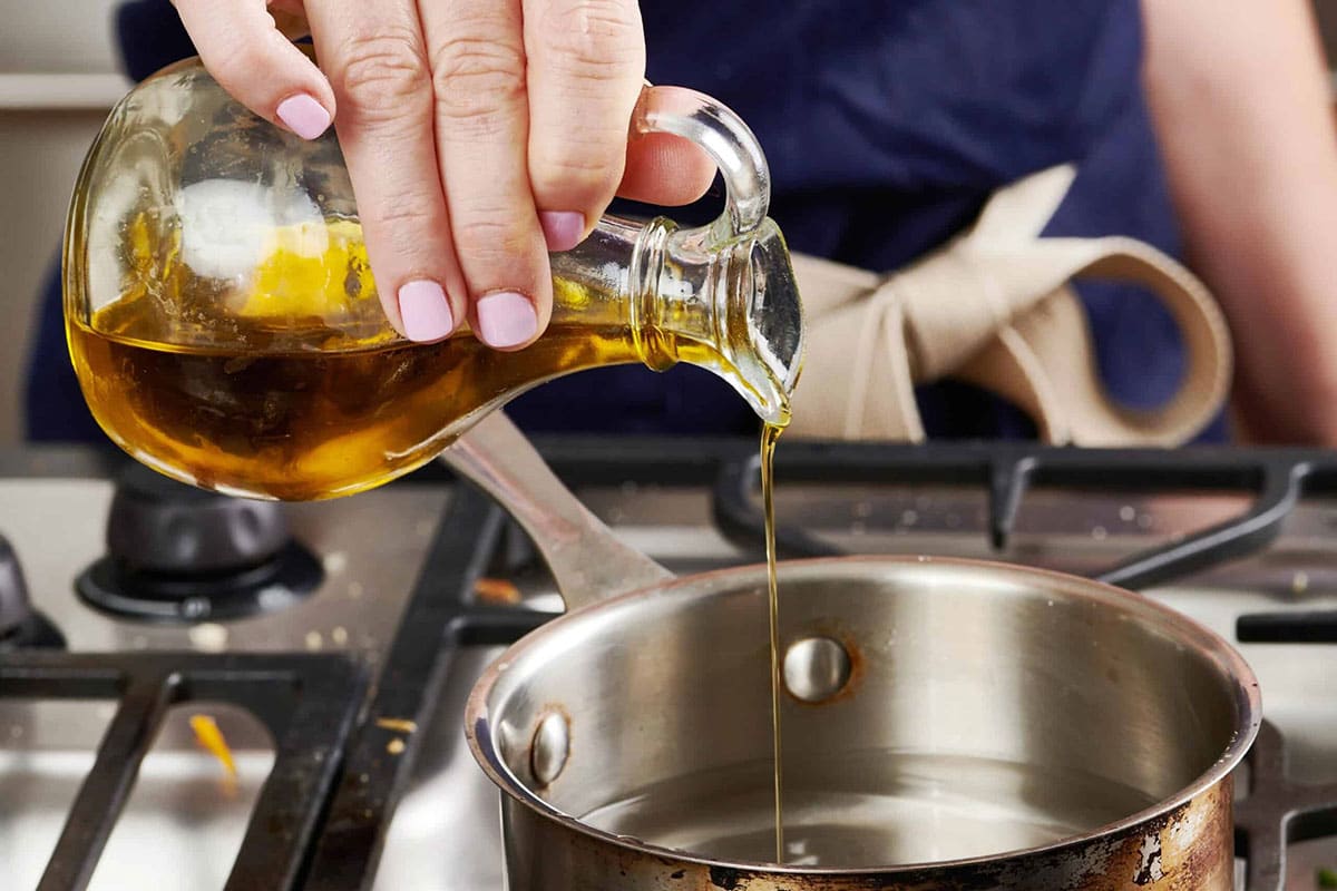 Pouring oil into pot of water on the stove.