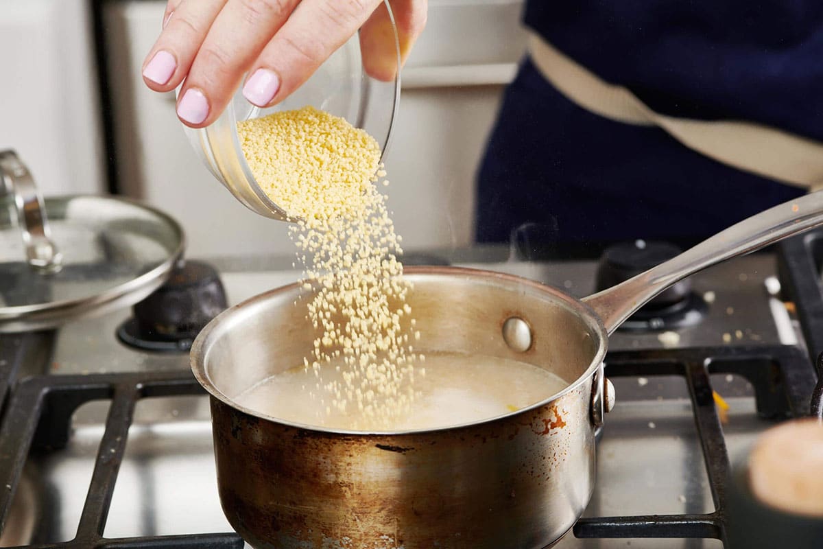 Pouring dry couscous into pan of boiling water.