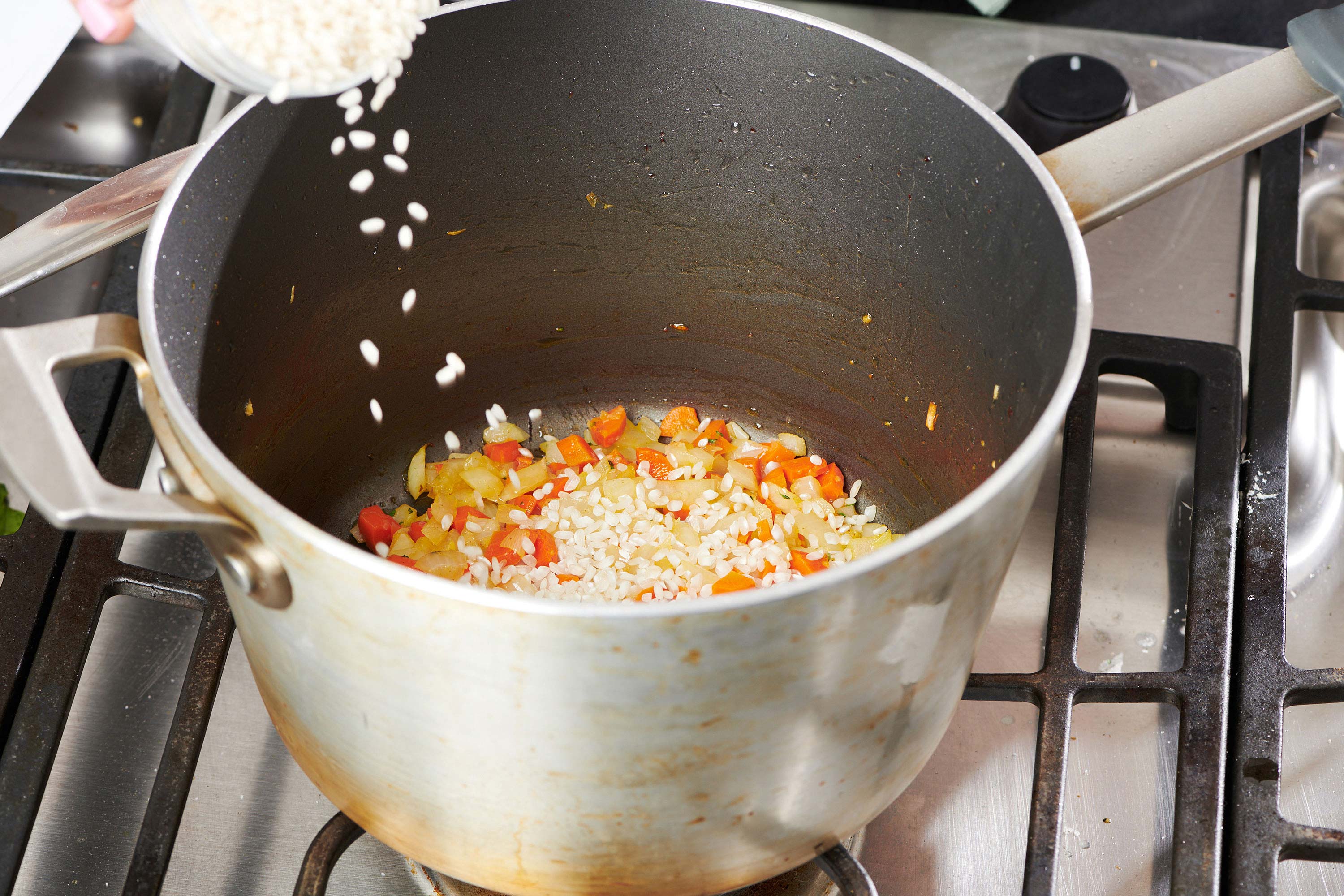 Rice pouring into a large pot with carrots and onions.