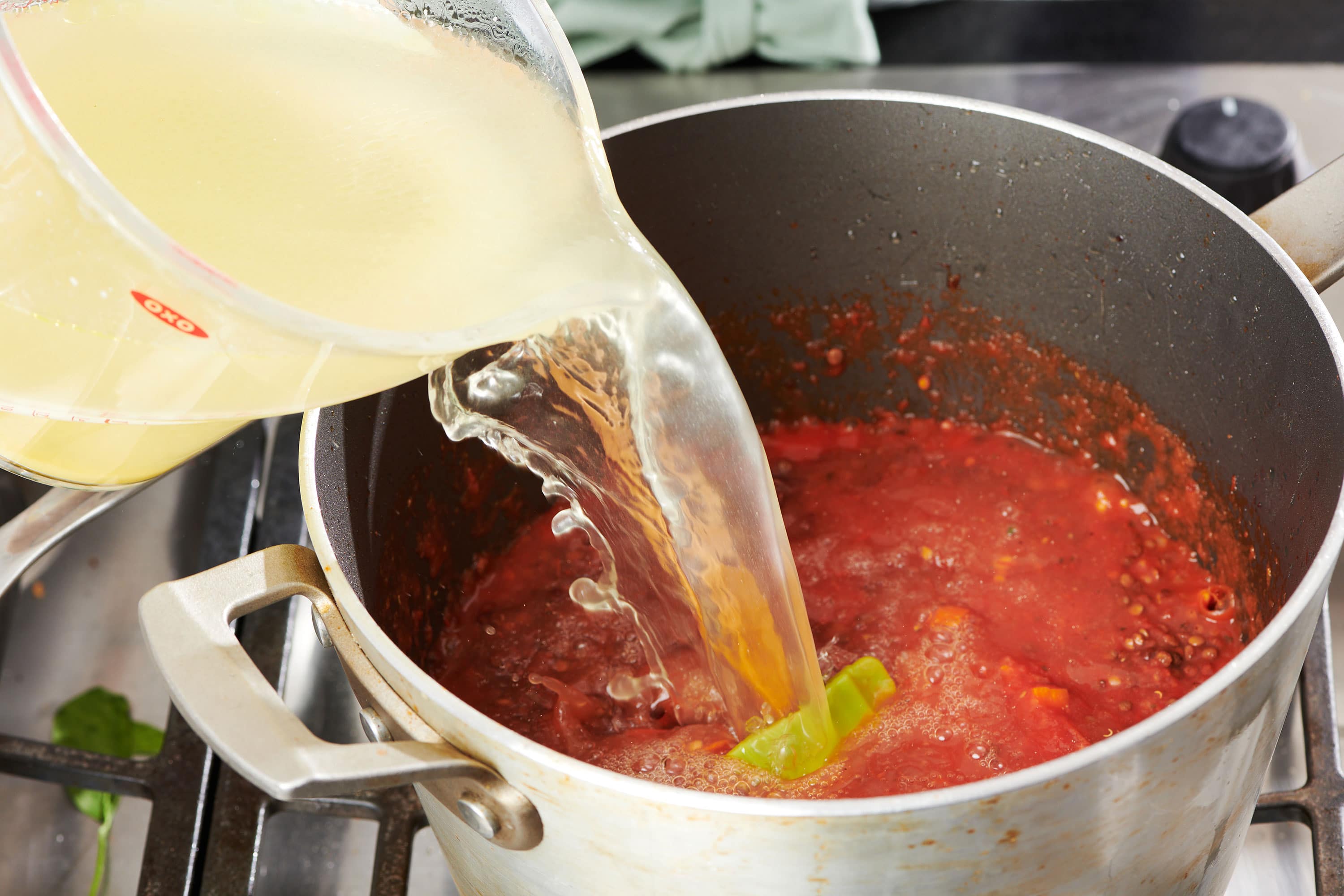Chicken broth pouring into a pan with crushed tomatoes and vegetables.