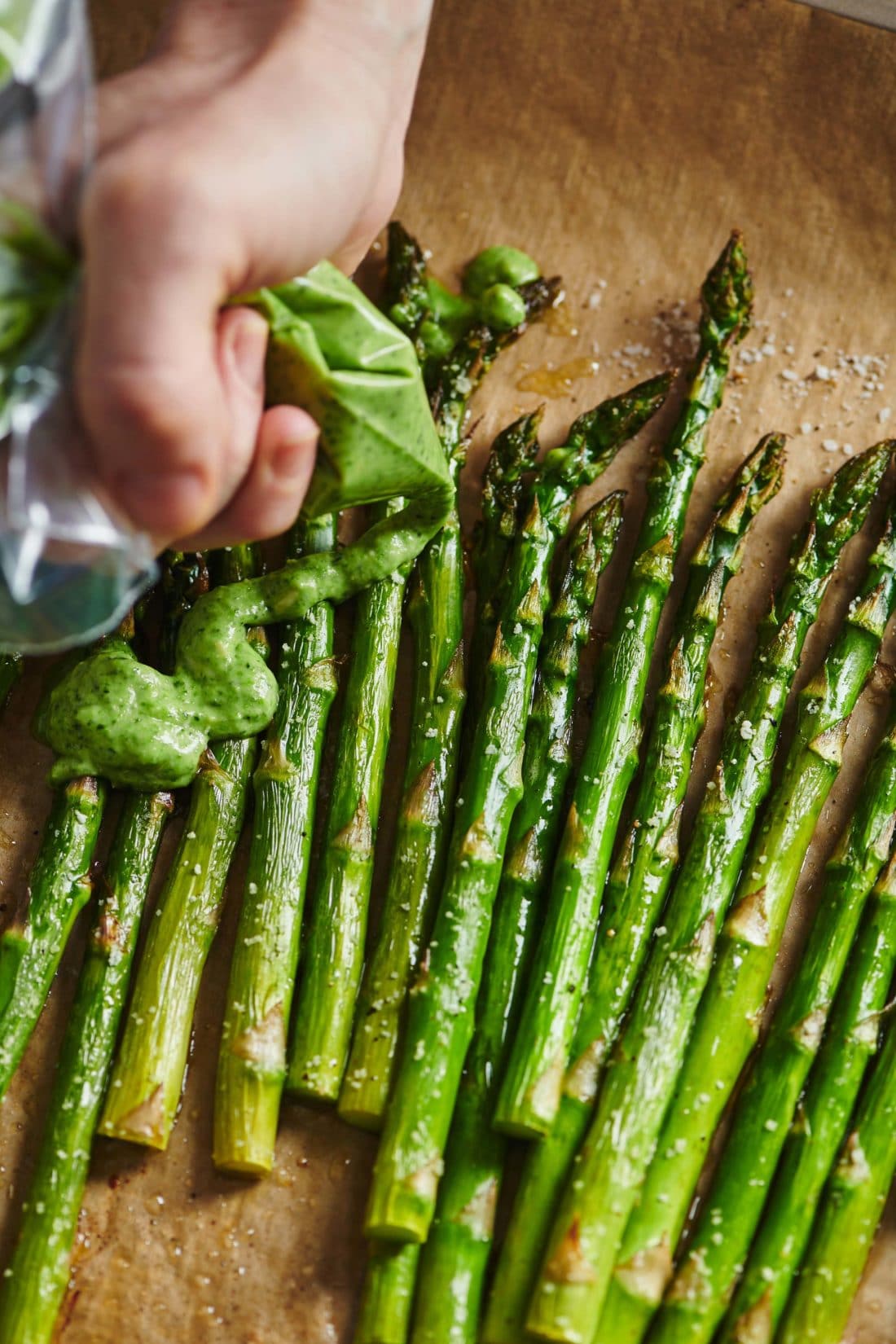 Woman topping Roasted Asparagus with Pesto Crème Fraiche.