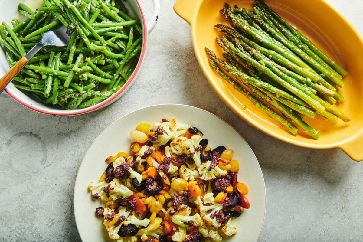 Dish of Roasted Asparagus with Pesto Crème Fraiche on a table with dishes of other vegetables.