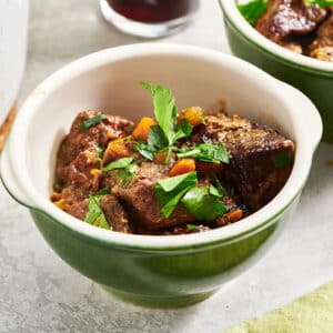 Beef stew in green bowls with parsley garnish.