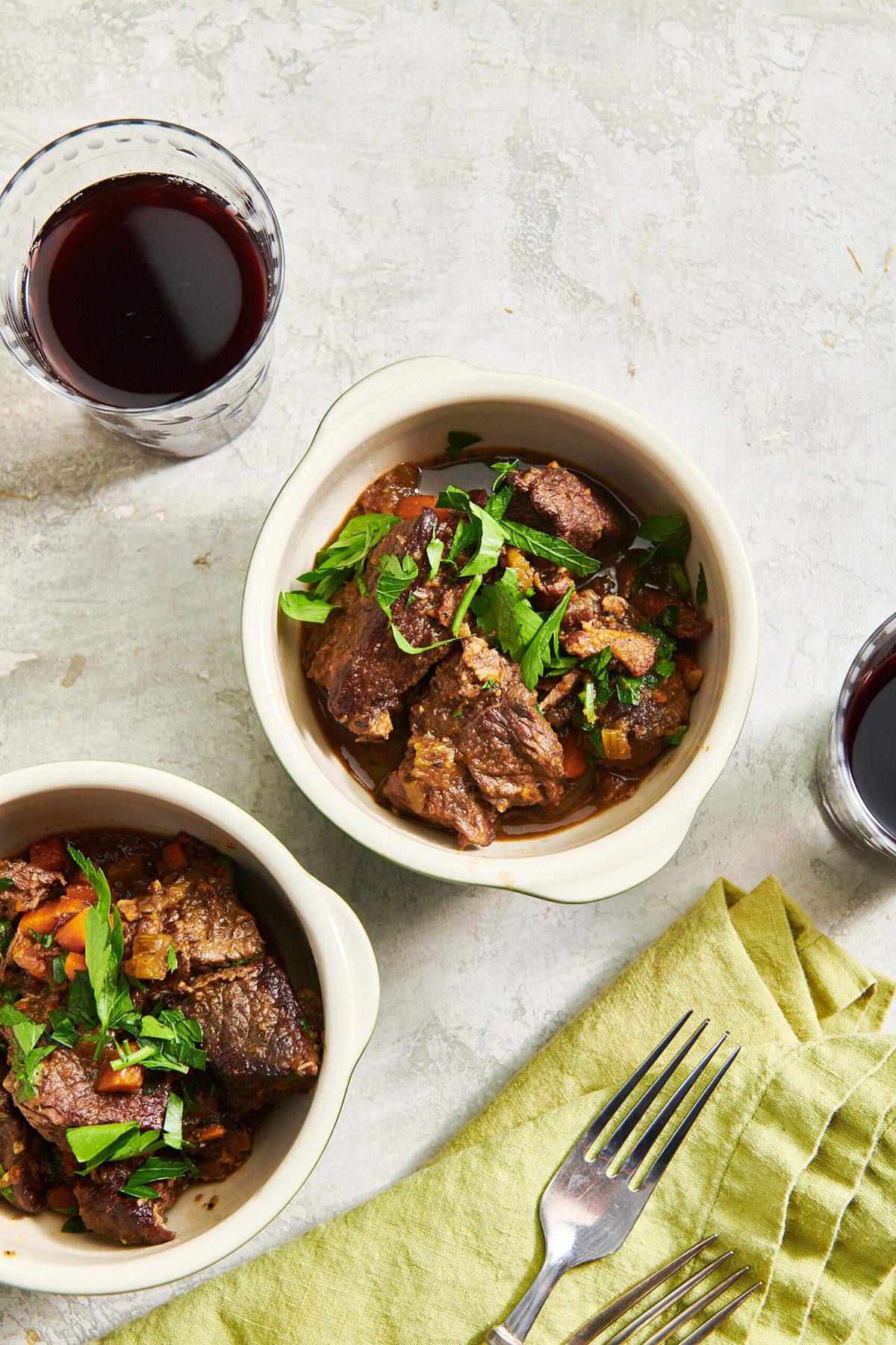 Two bowls of Beef Stew on table with drinks, silverware, and green napkin..