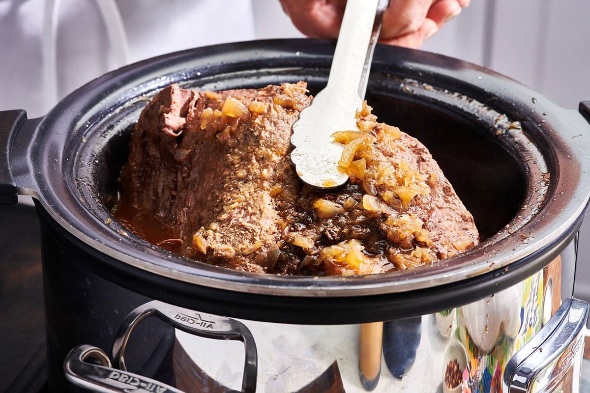 Tongs grabbing Pot Roast in a slow cooker.