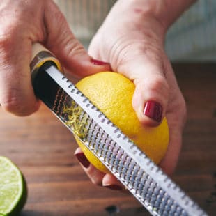 Woman zesting lemon with Microplane over wood cutting board.