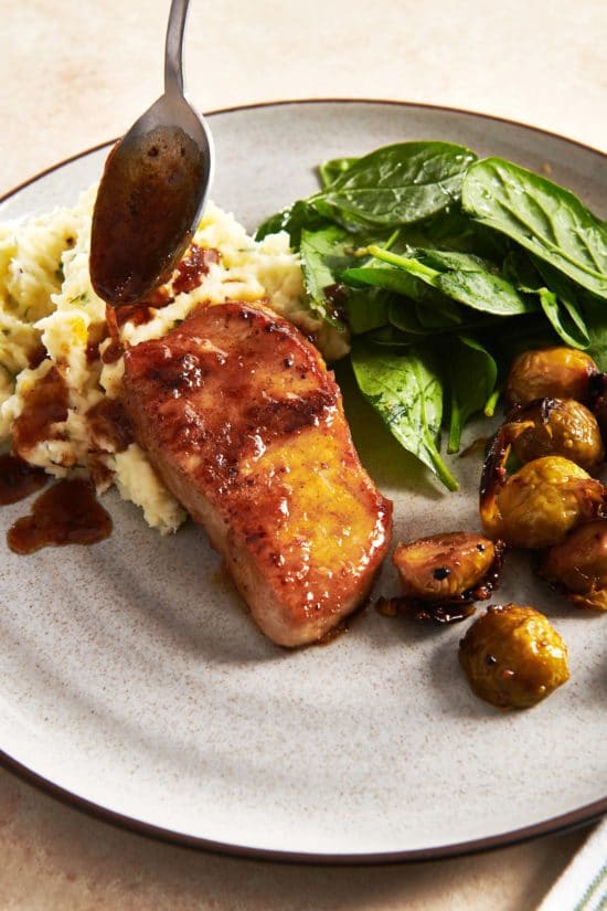 Drizzling honey and ginger glaze over pork chops on a plate with mashed potatoes and spinach