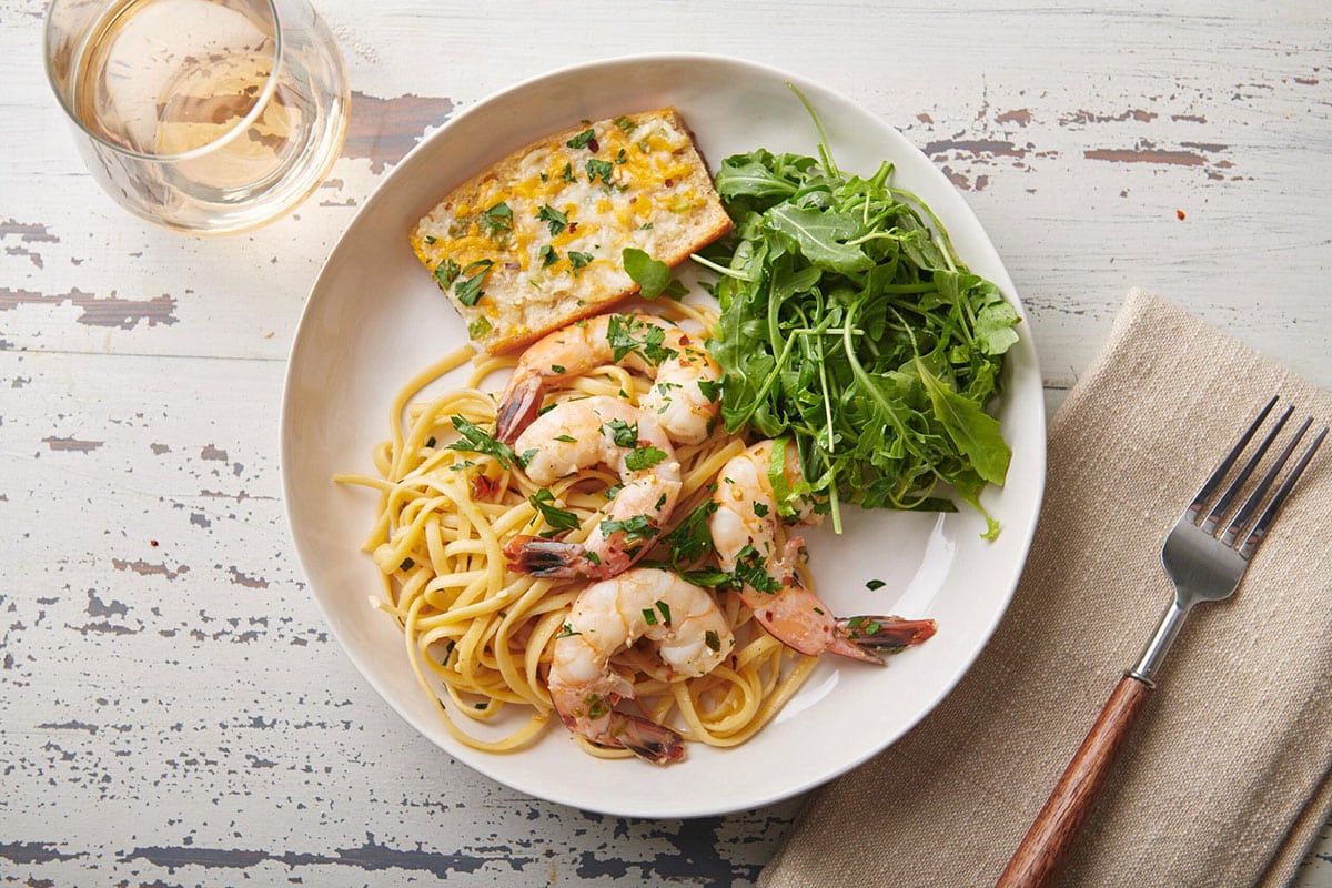 White plate with bread, greens, and Shrimp Scampi.