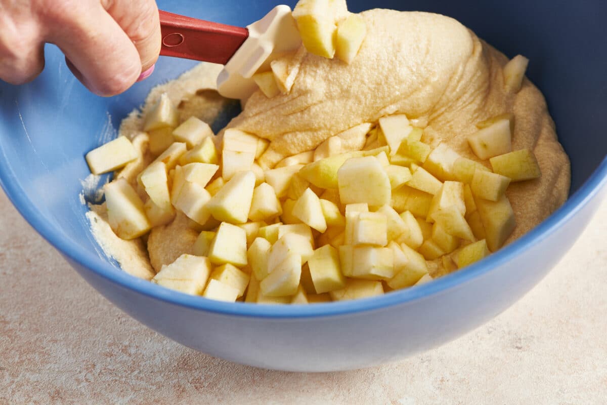 Spatula folding apple chunks into coffee cake batter.