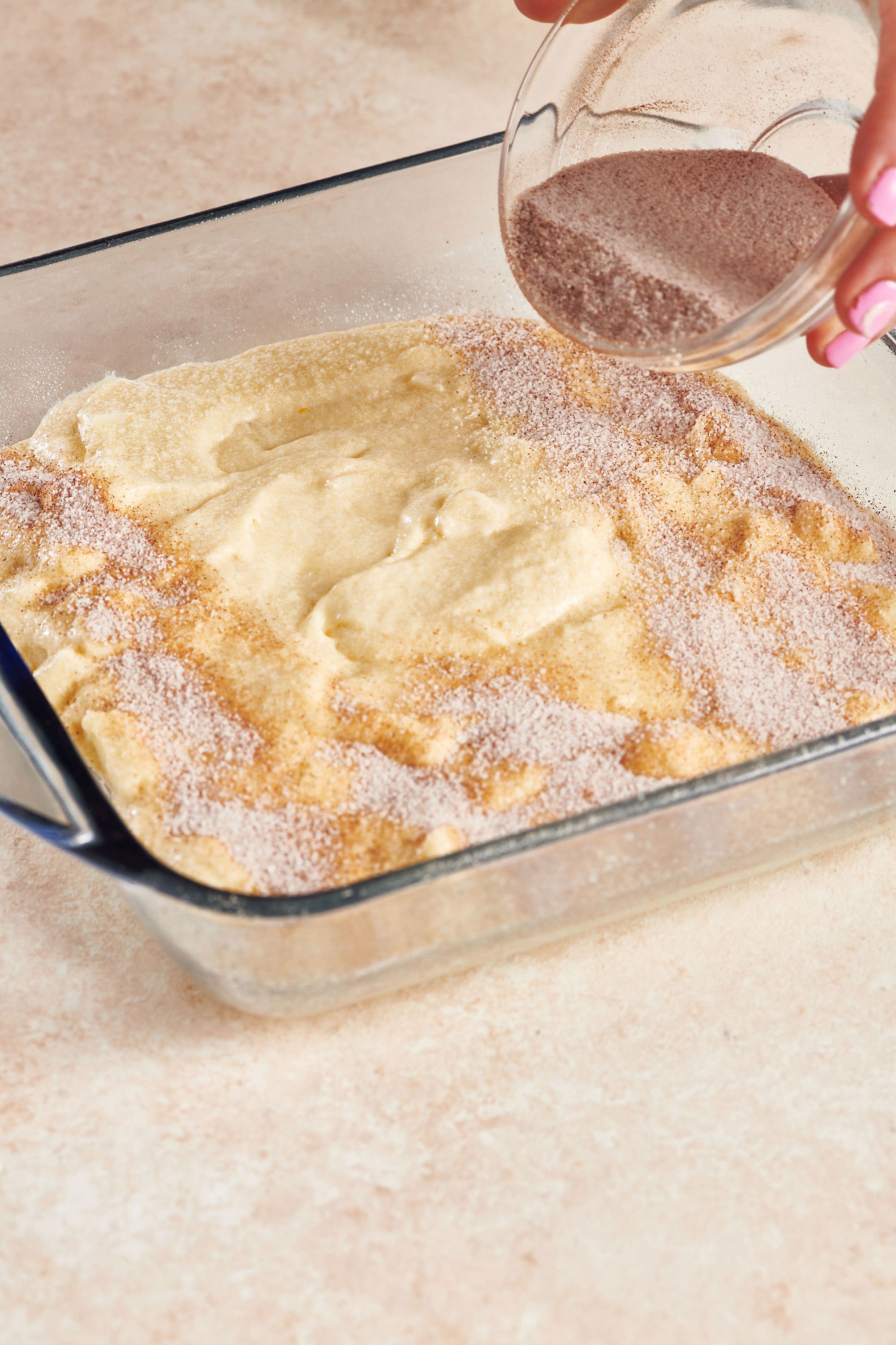 Woman sprinkling a sugar mixture onto an unbaked Apple Coffee Cake.