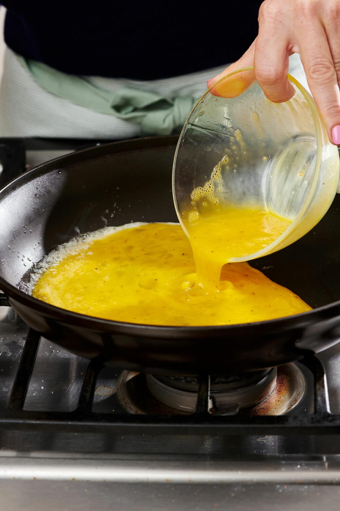Woman pouring whisked eggs into a skillet.
