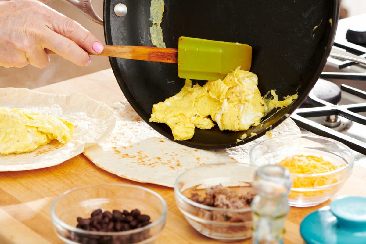 Spatula putting cooked eggs onto a tortilla.
