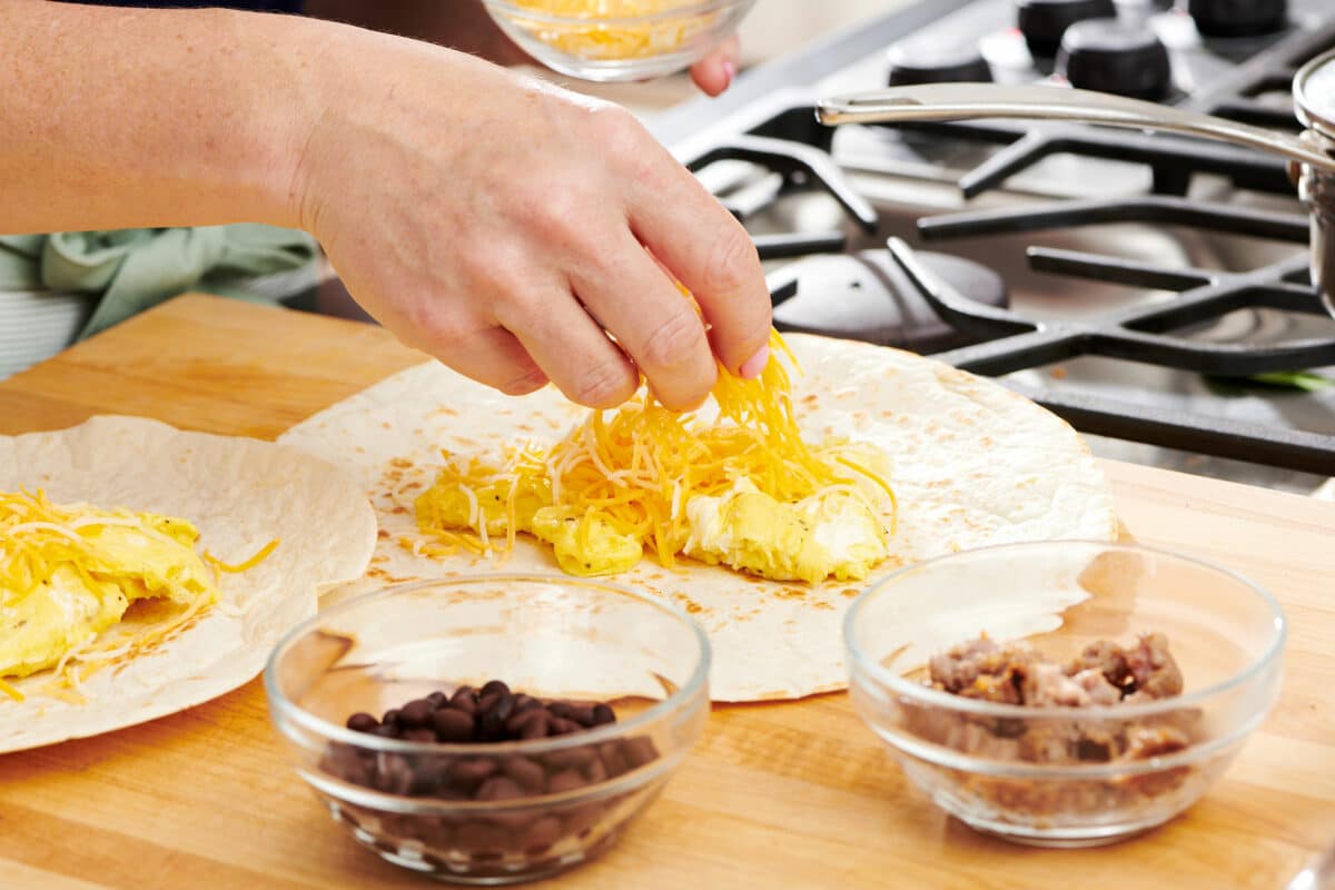 Woman placing shredded cheese onto eggs on a tortilla.